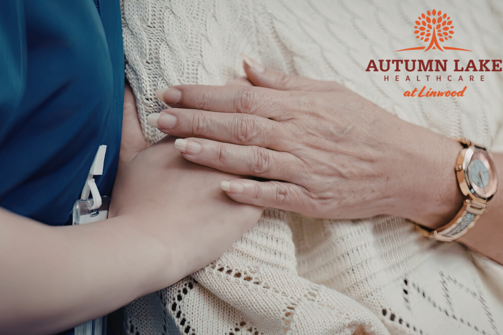 A healthcare worker comfortingly holding the hand of an elderly resident at Autumn Lake Healthcare at Linwood.
